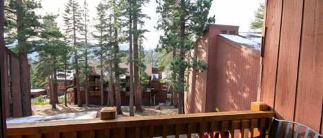 A wooden deck with a chair, overlooking a forested area with tall trees and a building in the background.