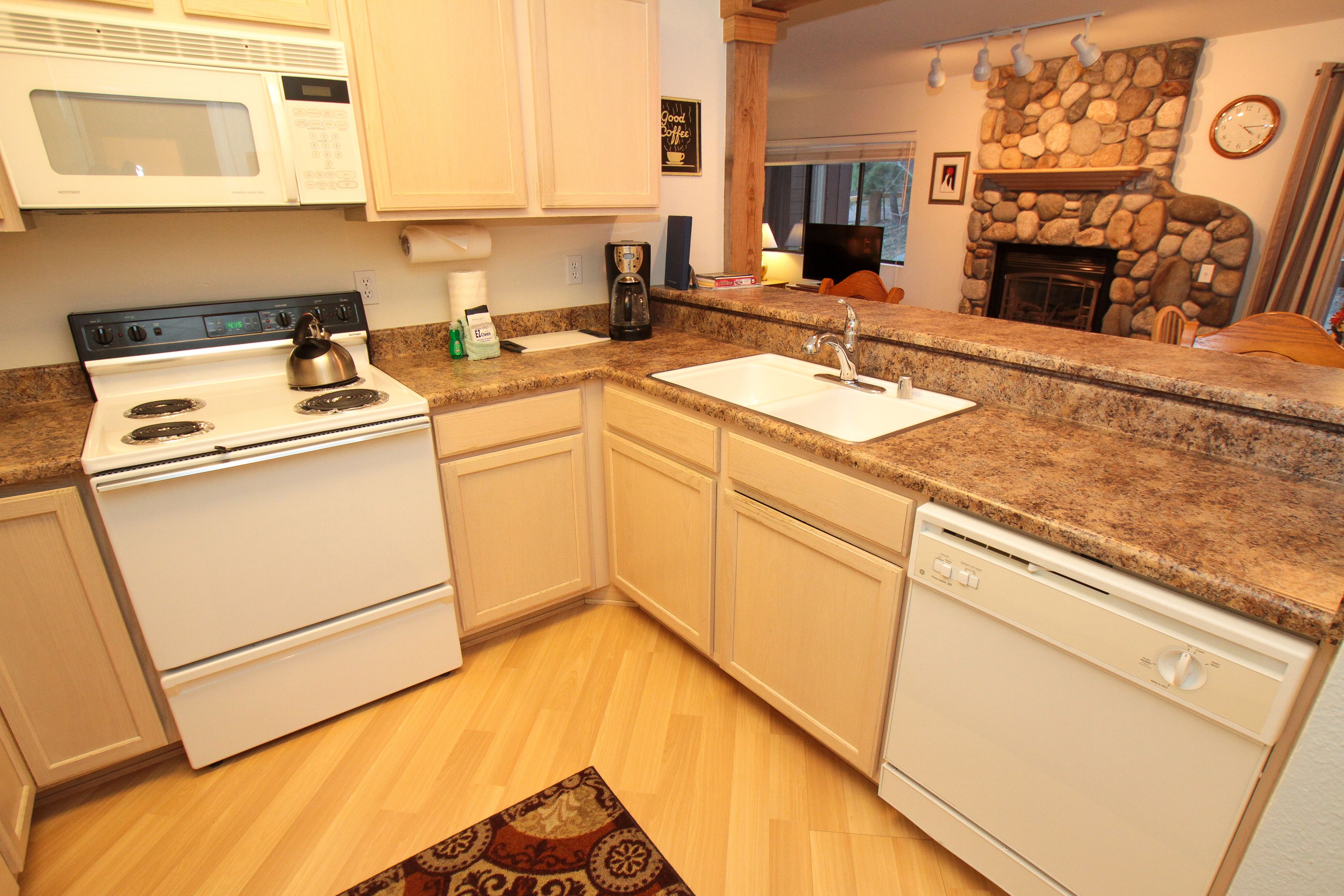 A compact kitchen with white appliances, a granite countertop, and a stone fireplace.