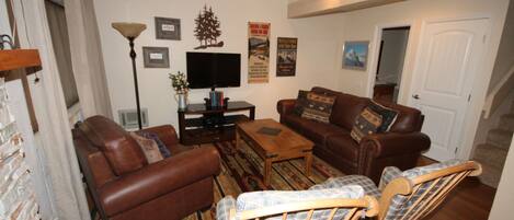 A living room with a brown leather sofa, a wooden coffee table, and a plaid armchair.