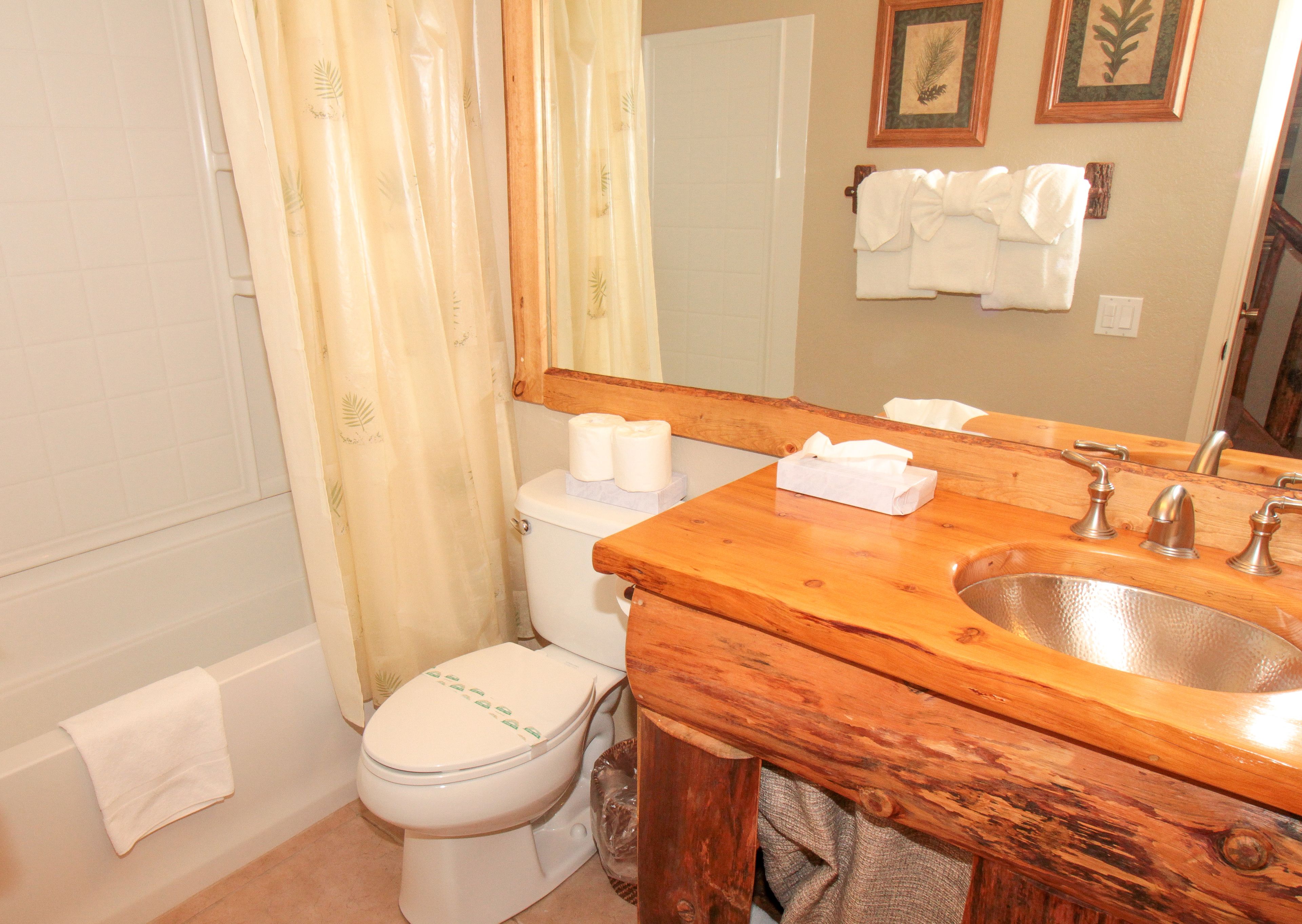 A bathroom with a wooden vanity, a sink, a toilet, and a shower curtain.