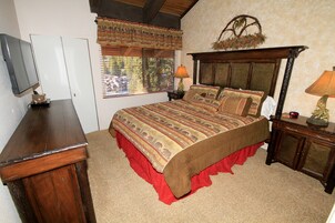 A bedroom with a bed, a wooden nightstand, a TV, a wardrobe, and a window with curtains.