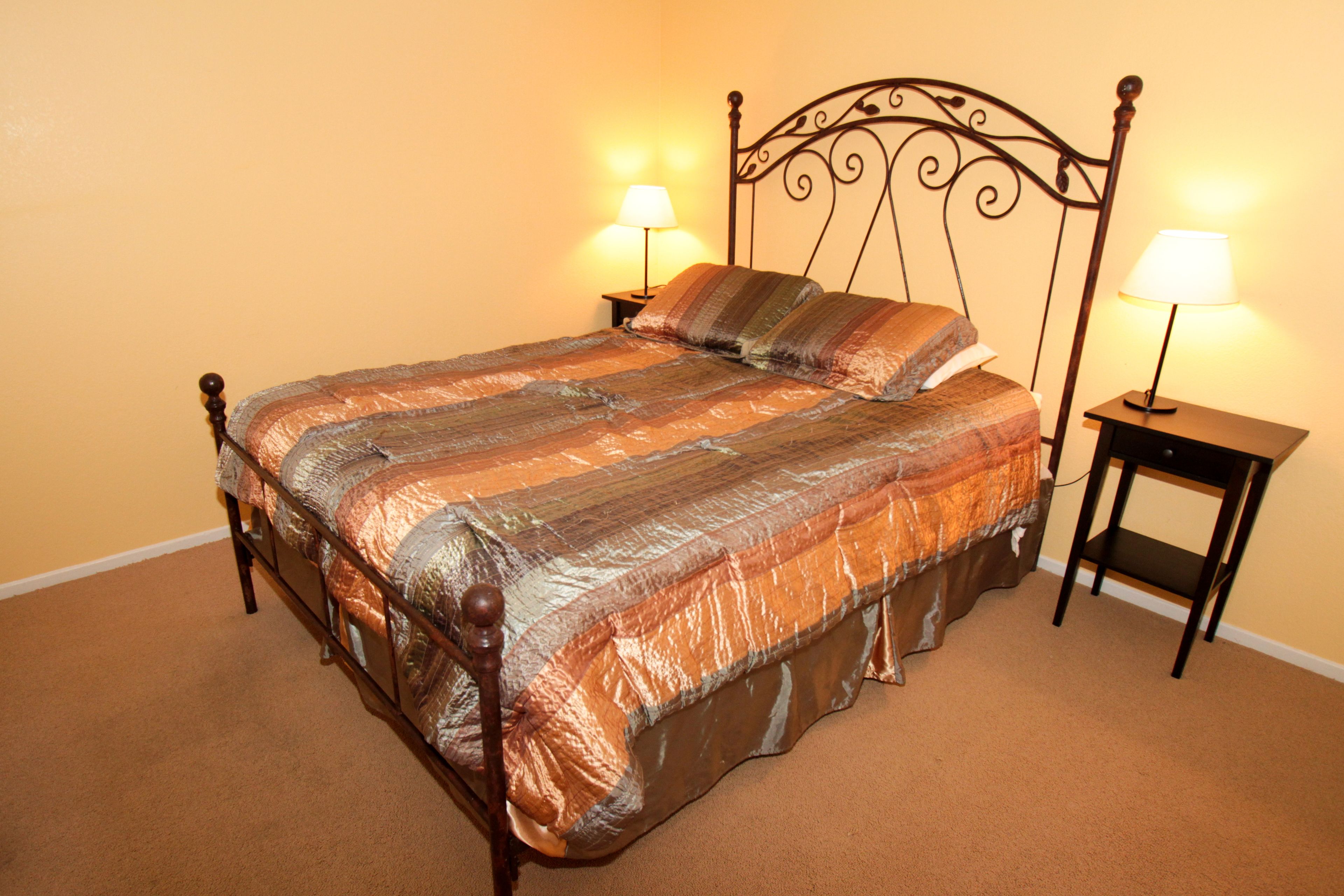 A neatly made bed with a striped bedspread, two bedside lamps, and a wooden headboard.