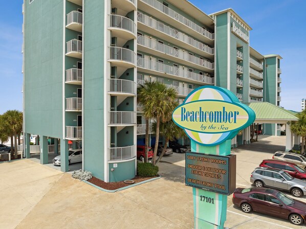 A multi-story hotel with balconies, a sign reading "Beachcomber by the Sea," and a parking area with several cars. - Beachcomber Beachfront Hotel, a By The Sea Resort (Panama City Beach)