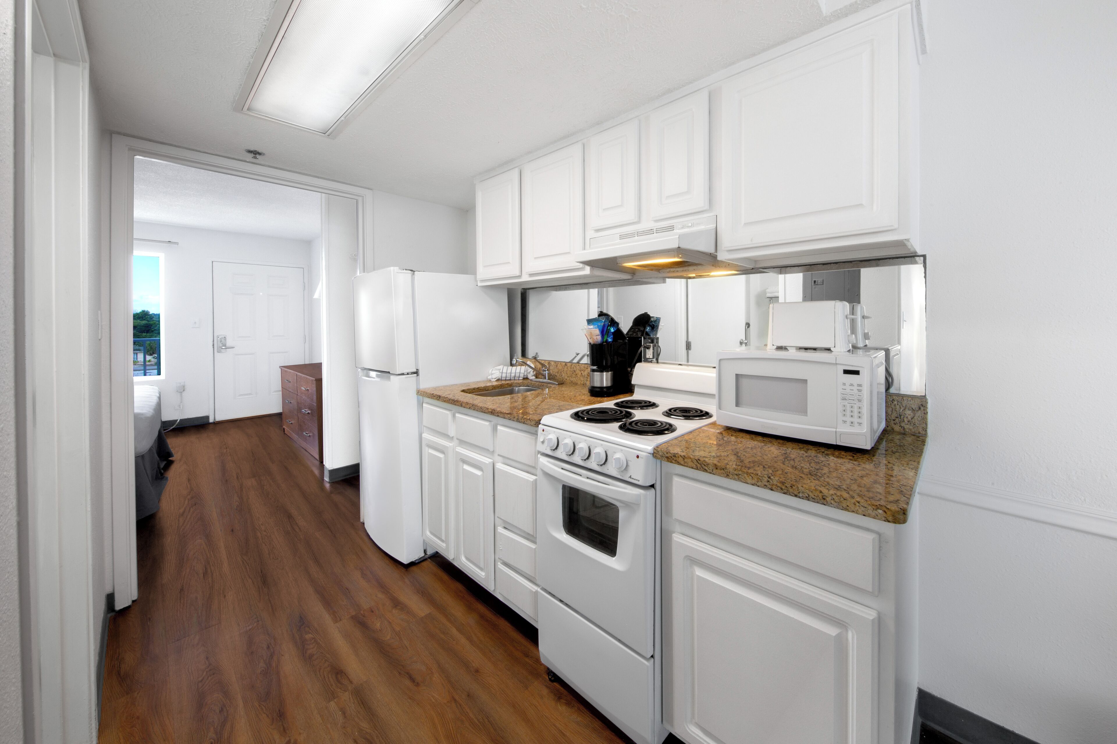 A kitchen with white cabinets, a stove, a microwave, and a countertop with a sink.