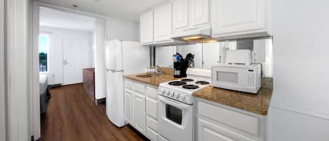 A kitchen with white cabinets, a stove, a microwave, and a countertop with a sink.