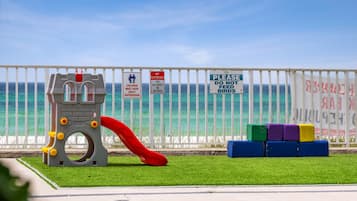 Children can play safely in this enclosed playground, featuring a slide and climbing structure, with the ocean nearby.