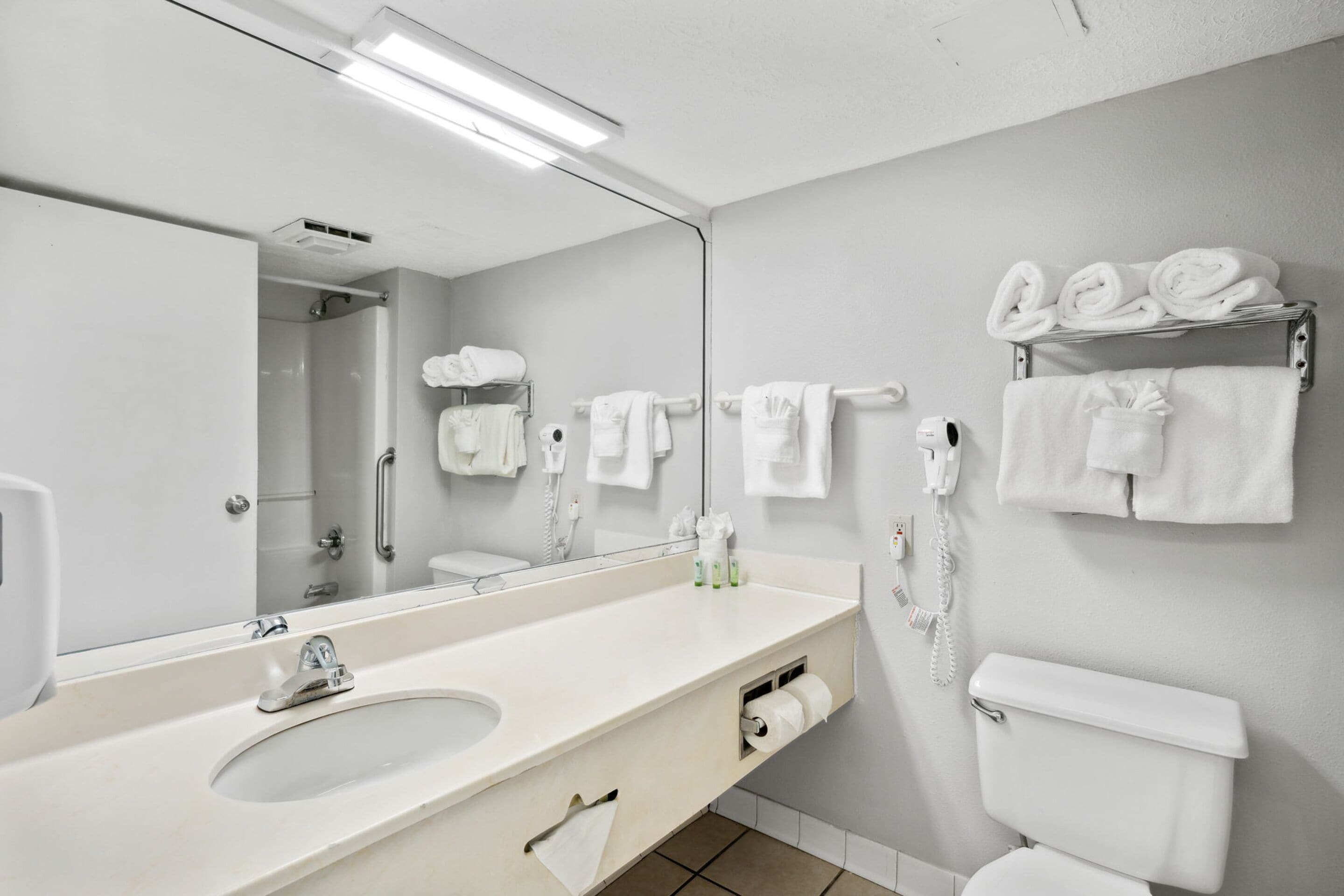 A modern bathroom with a large mirror, a sink, a toilet, and towel racks.