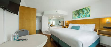 Une chambre d’hôtel avec un lit, un bureau, une chaise, une télévision, une salle de bain et un tableau au mur.