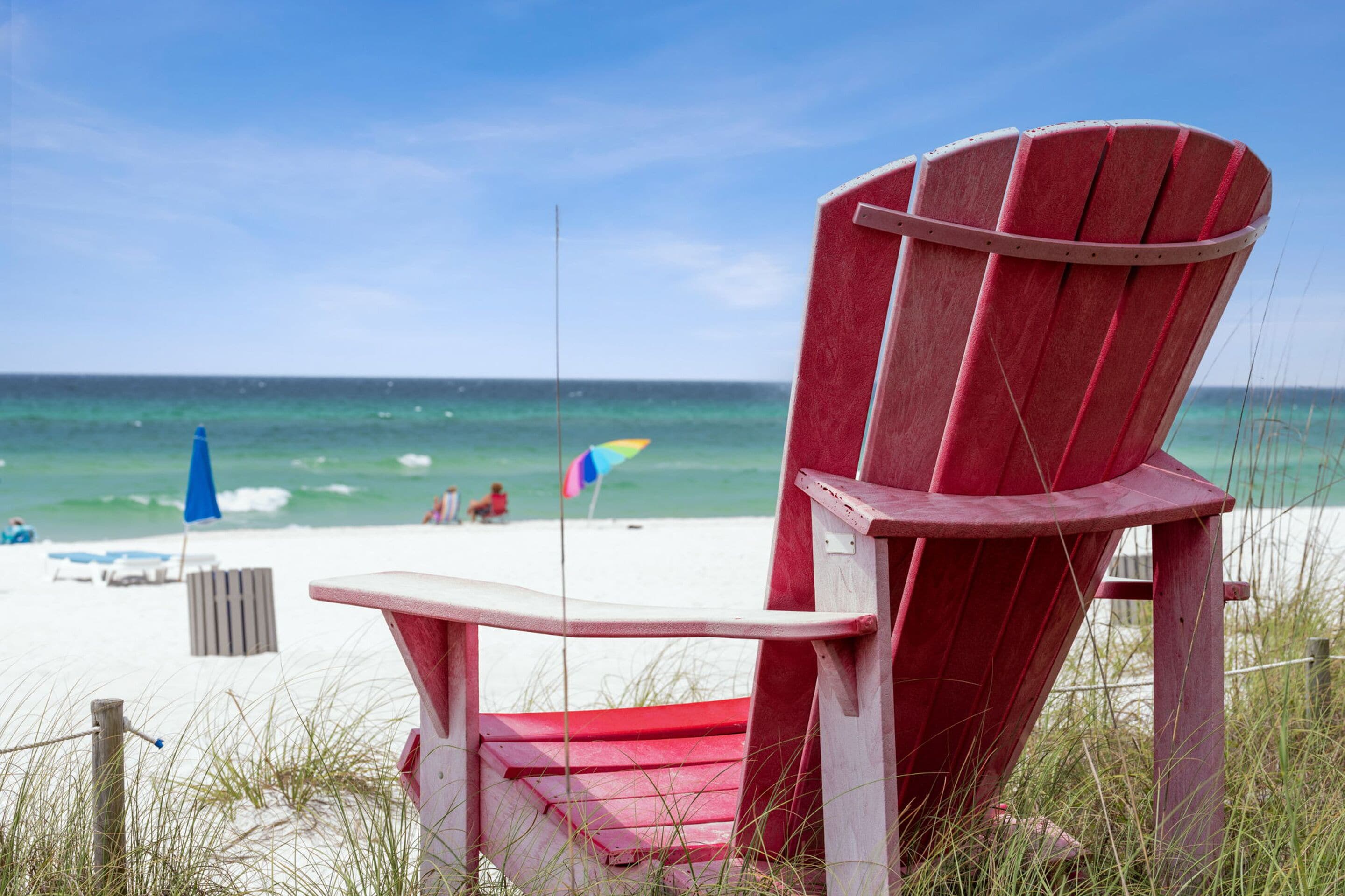 Una silla de playa roja con vista al océano y la playa de fondo.