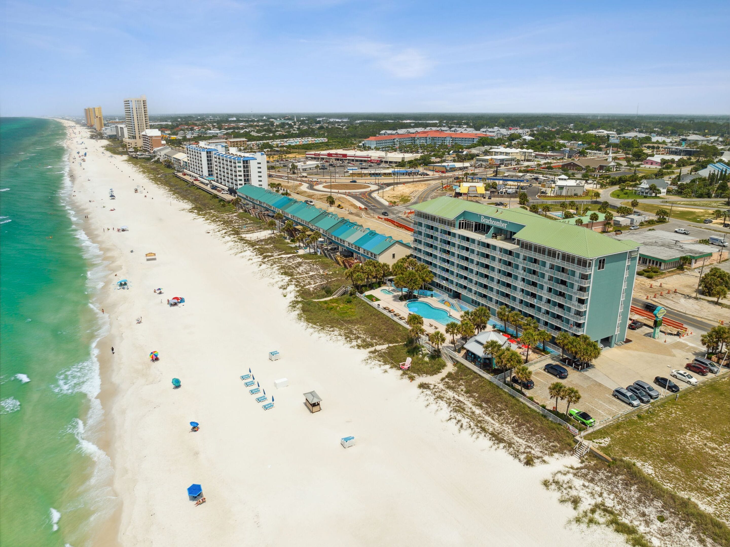 Et hotel ved stranden med flere etager, en swimmingpool og et strandareal med parasoller.