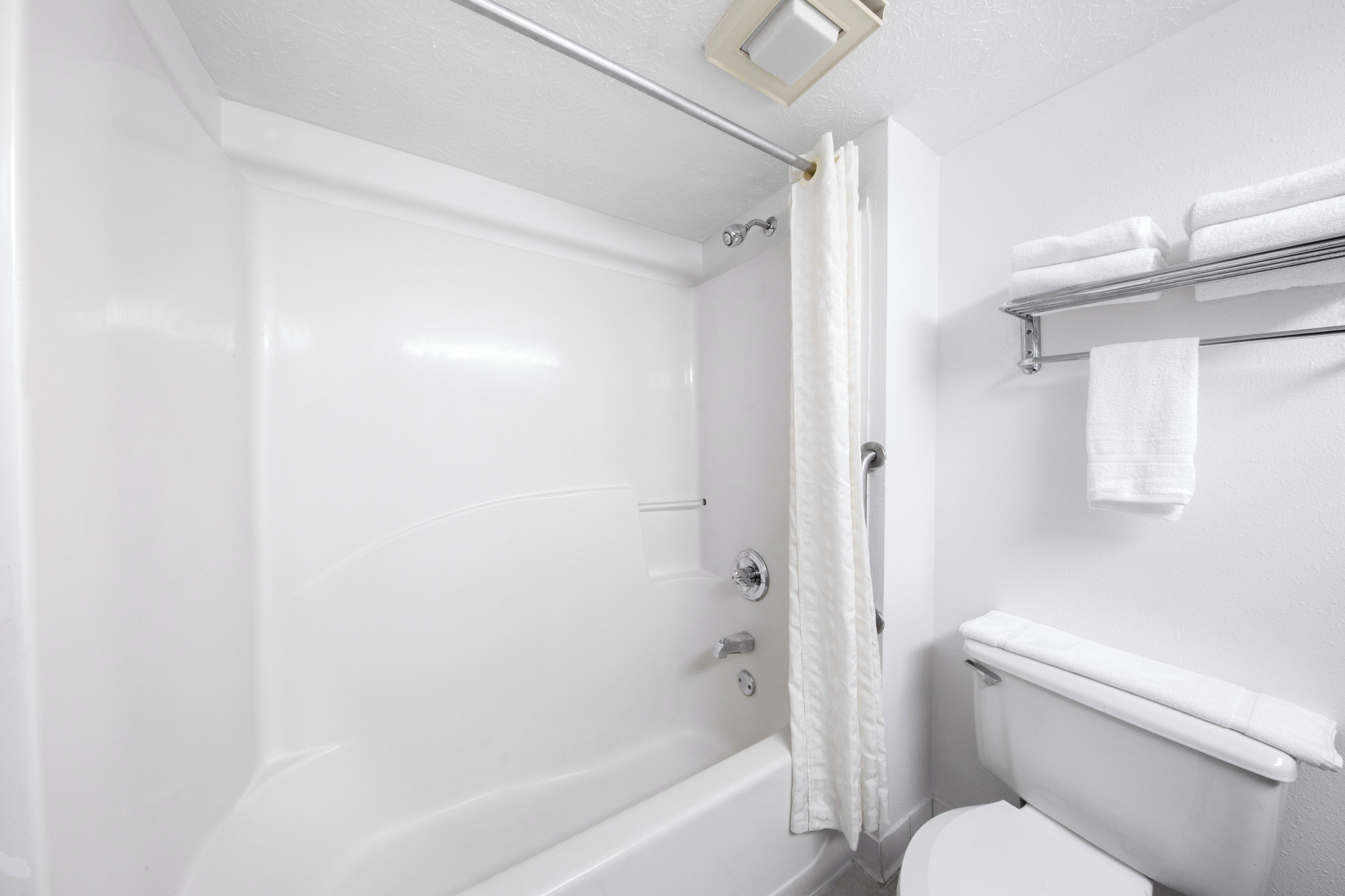 A bathroom with a white bathtub, a toilet, and a towel rack with folded towels.