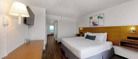 A hotel room with a bed, bedside table, lamp, TV, and a painting on the wall.
