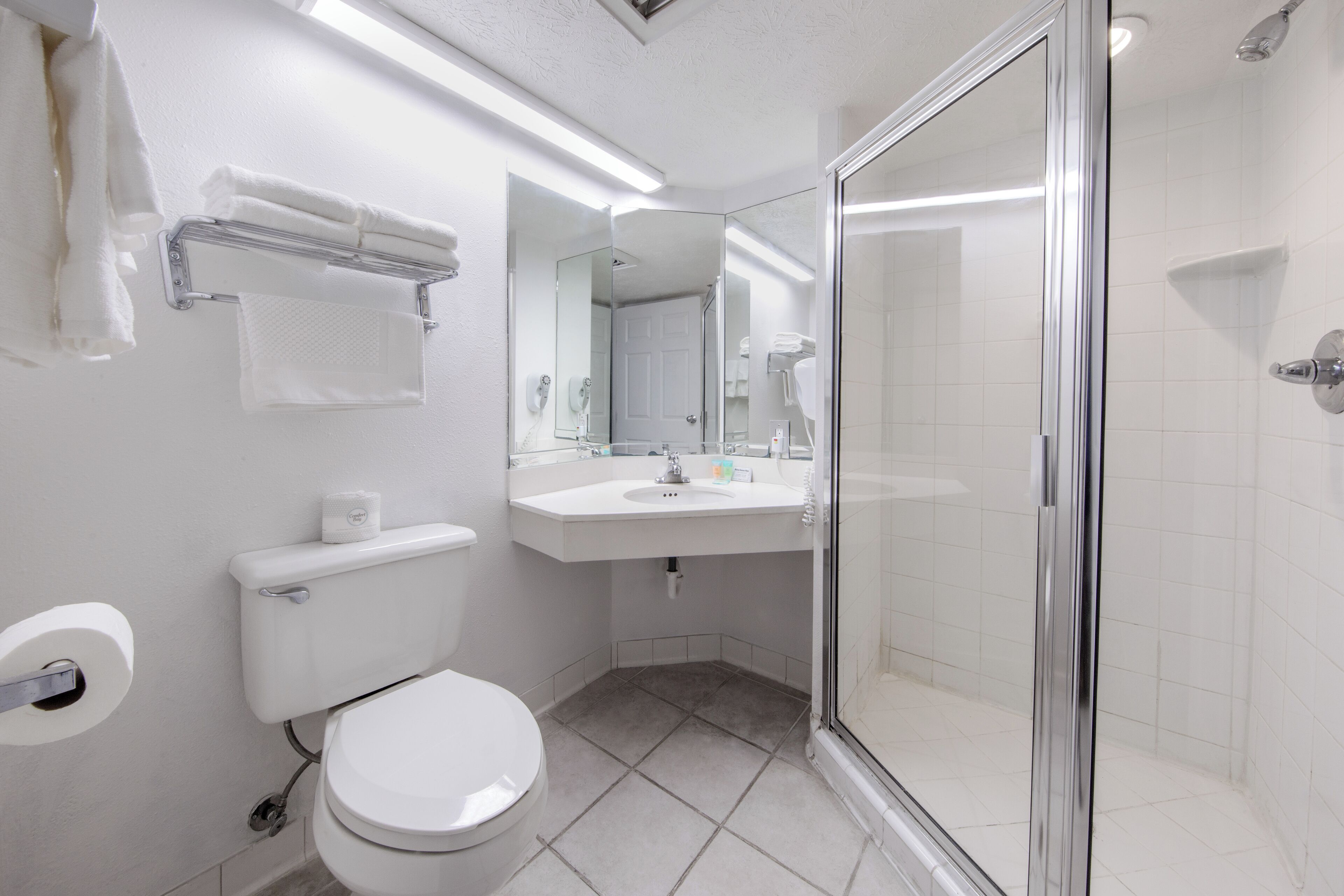 Baño con inodoro, lavabo y ducha con mampara de vidrio.