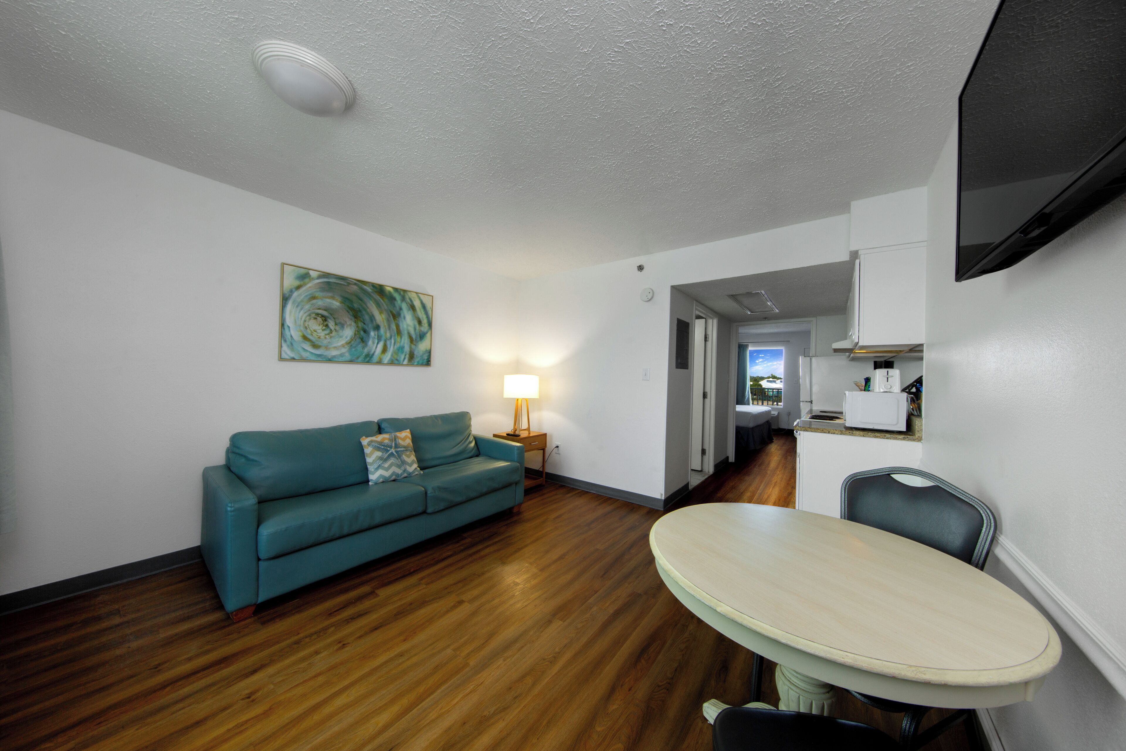 A living room with a teal sofa, a round table, and a TV mounted on the wall.