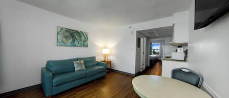 A living room with a teal sofa, a round table, and a TV mounted on the wall.