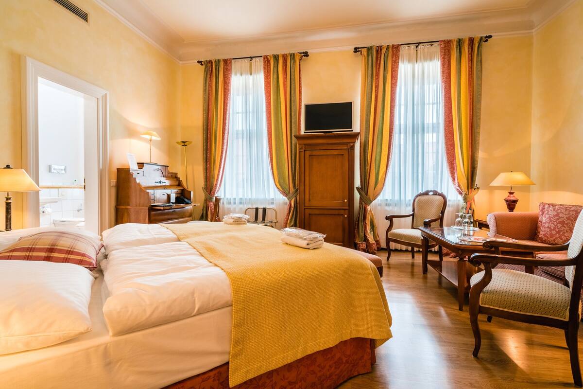 Una habitación de hotel con una cama, dos sillas, una mesa, un televisor y cortinas.