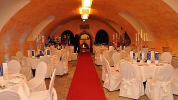 A banquet hall with white tablecloths, round tables, and chairs, a red carpet, and a high arched ceiling.