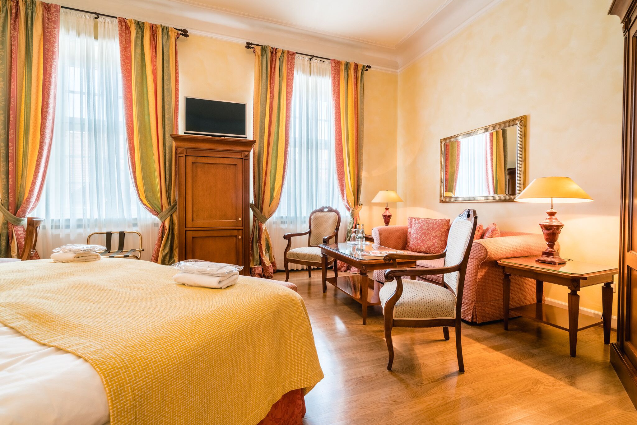 A hotel room with a large bed, a desk, a chair, a sofa, a television, and a mirror.