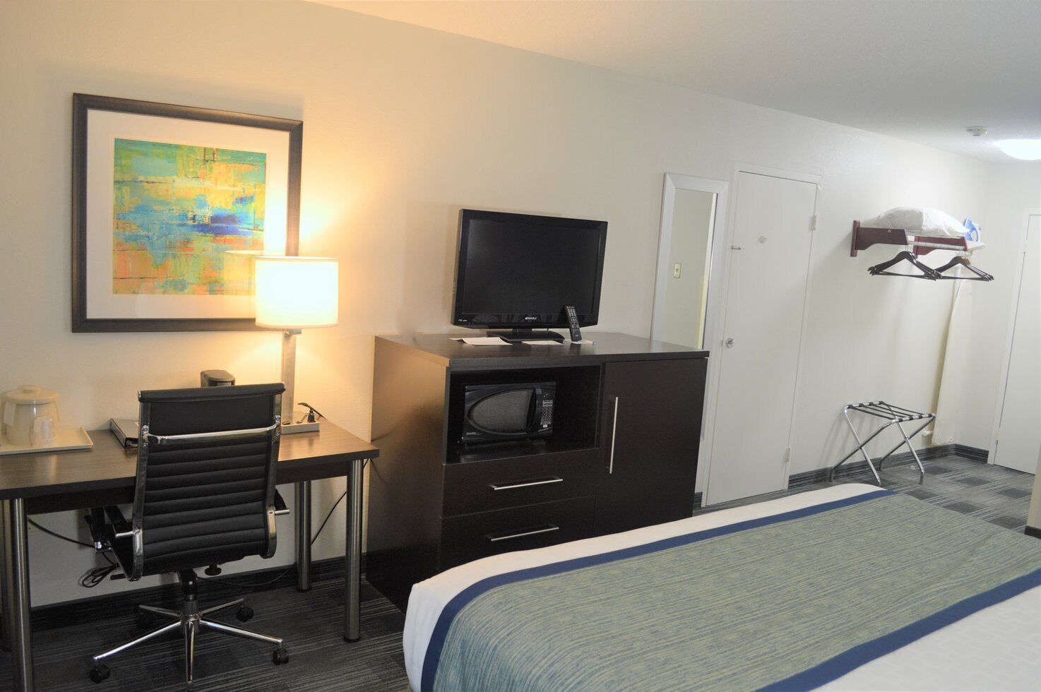 A hotel room with a bed, desk, chair, television, and wardrobe.