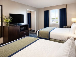 Habitación de hotel con cama, televisión, escritorio con cajones, ventana con cortinas y vistas al exterior.
