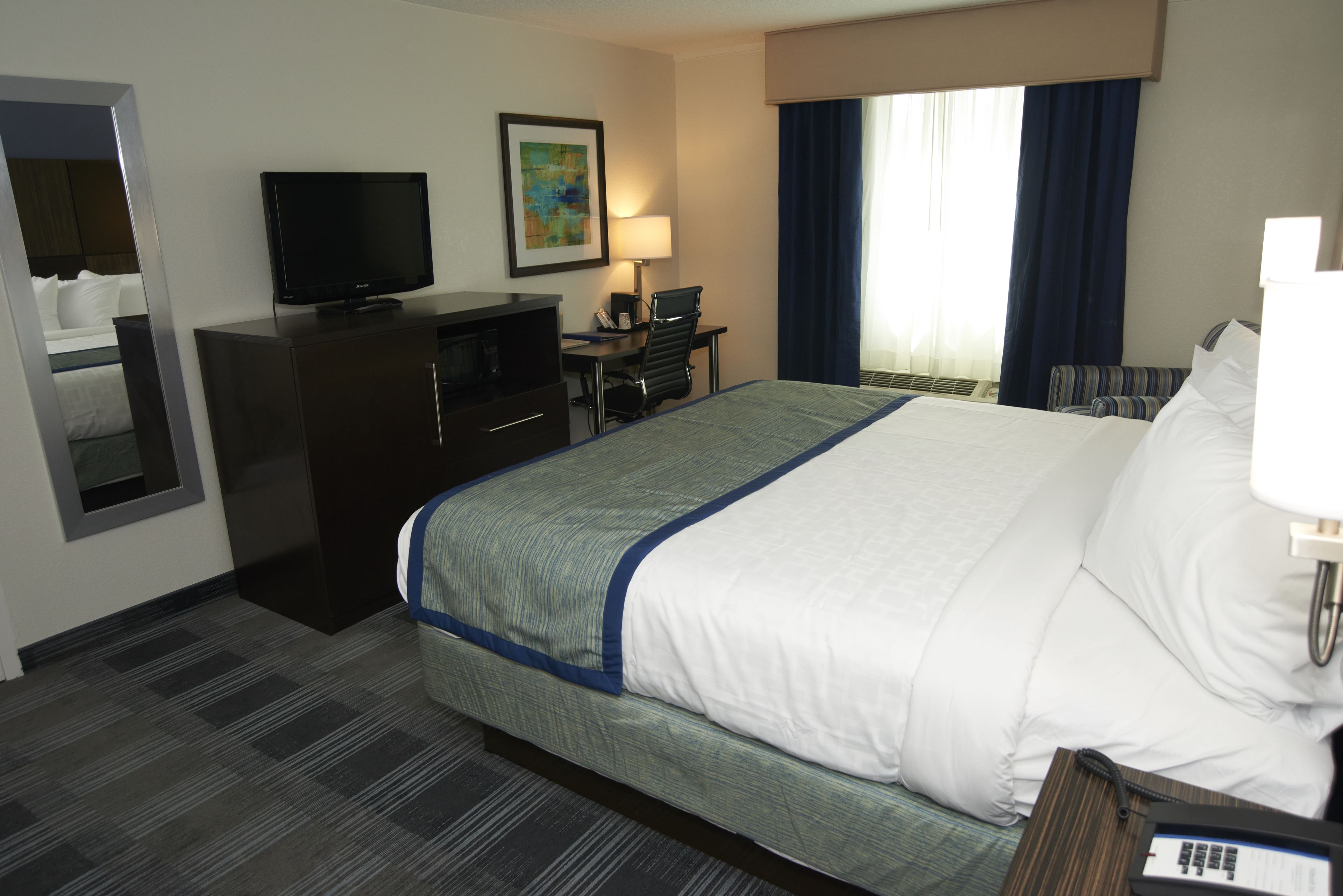 Une chambre d’hôtel avec un grand lit, un bureau avec un ordinateur, une télévision et une fenêtre avec des rideaux.