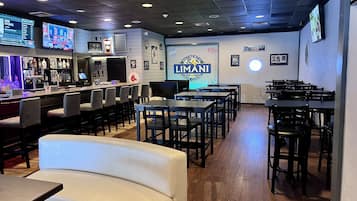 Un interior de restaurante con asientos de bar, mesas y un mostrador con pantalla.