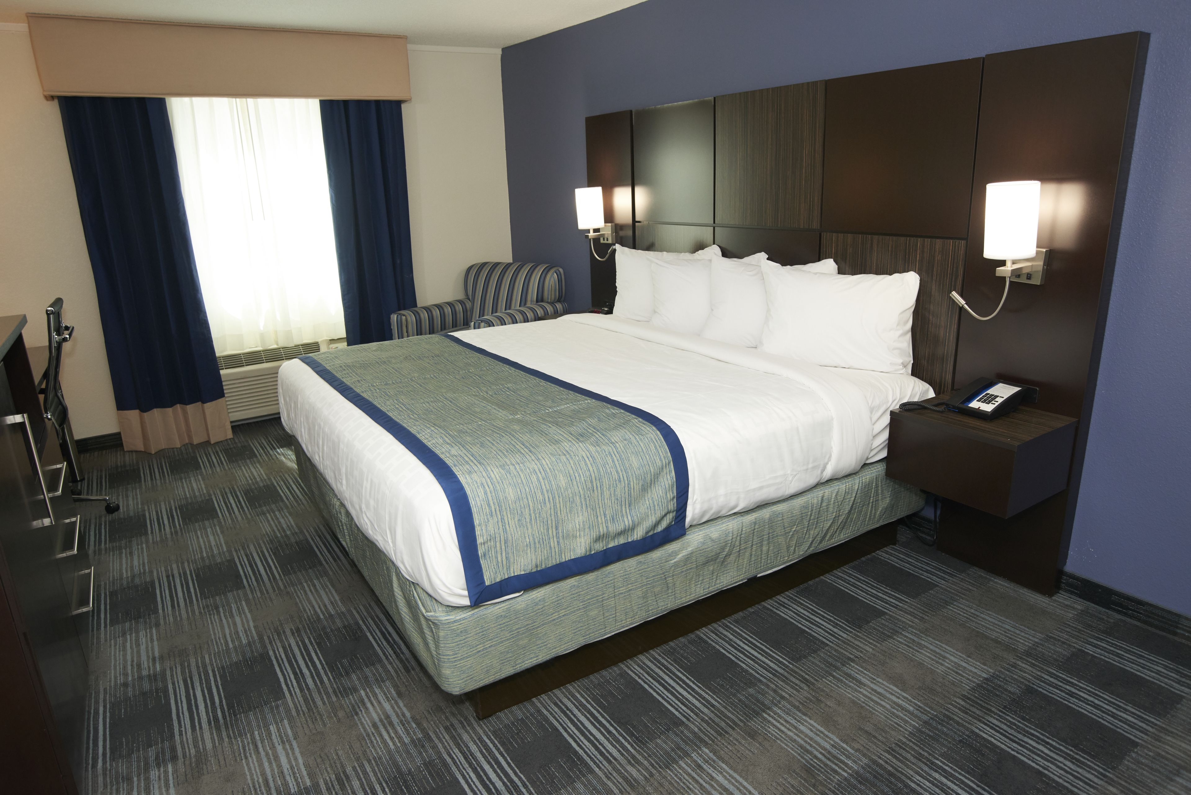 A hotel room with a large bed, two bedside tables, a chair, and a desk with a lamp.