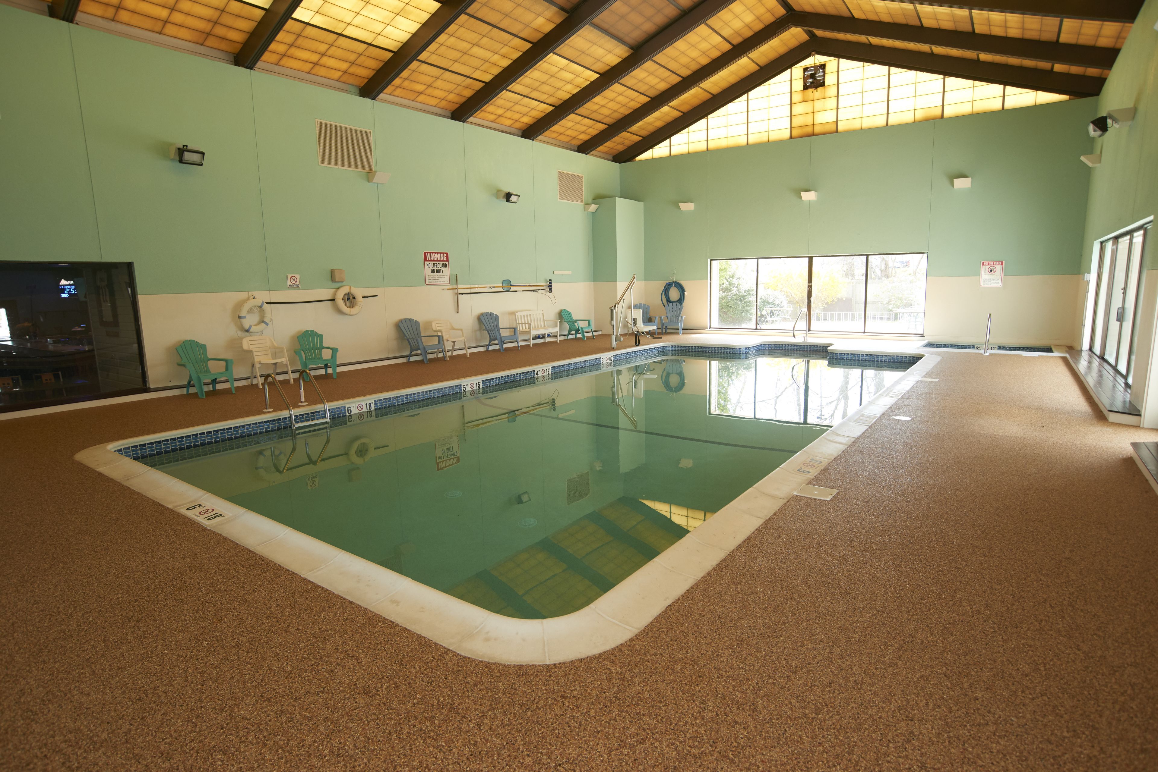 An indoor swimming pool with a tiled floor, safety signs, and a wooden ceiling.