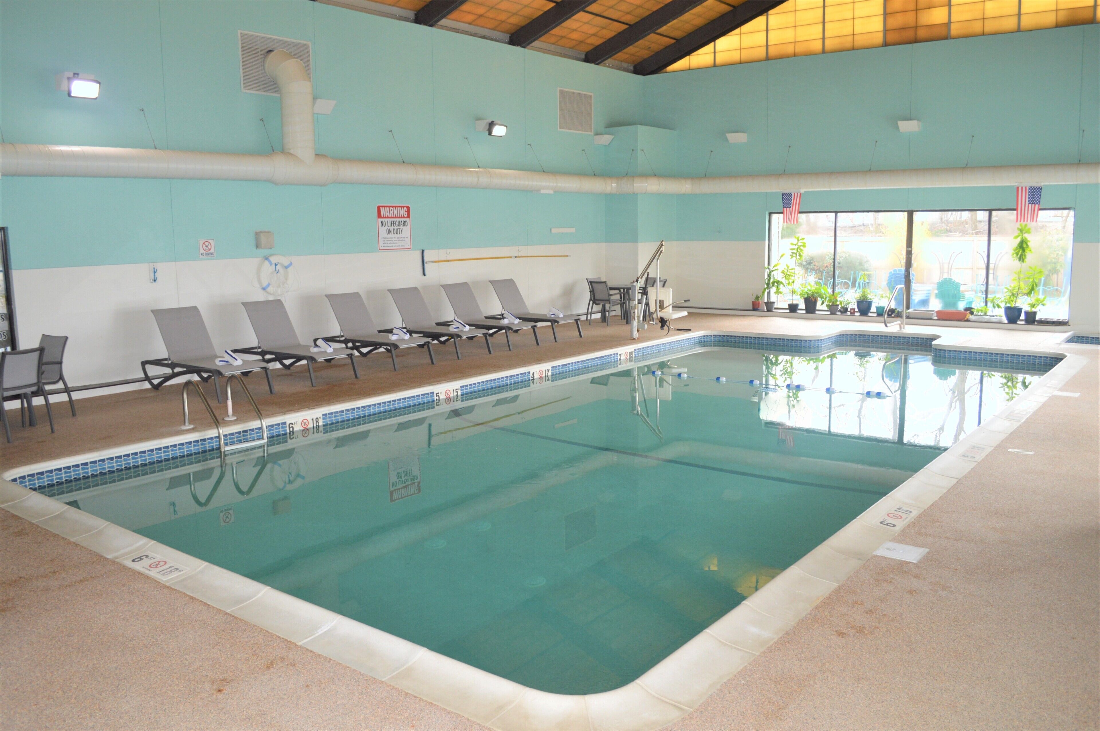 An indoor swimming pool with clear water, multiple lounge chairs, and American flags.