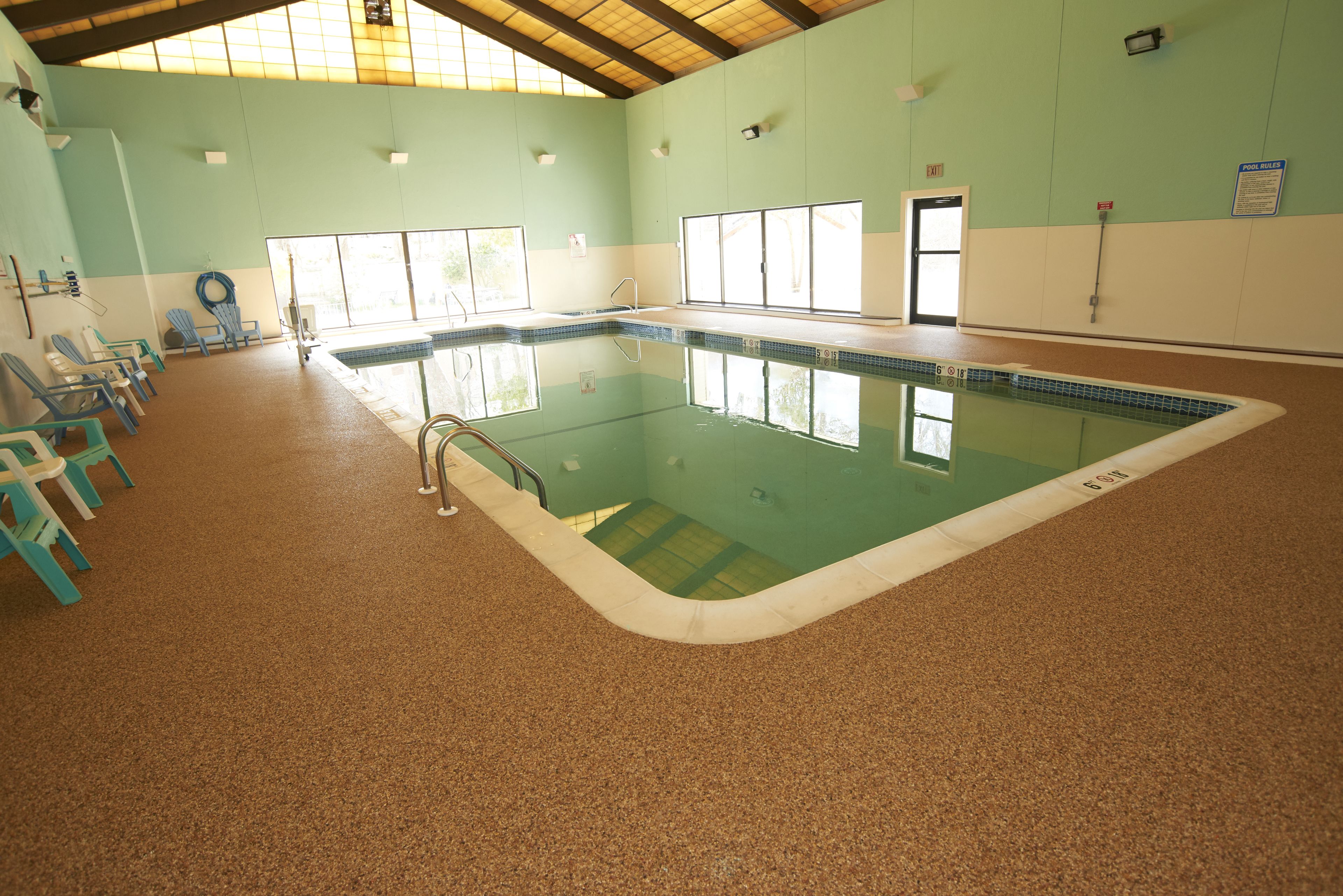 An indoor swimming pool with a tiled floor, a diving board, and a set of blue chairs along the wall.