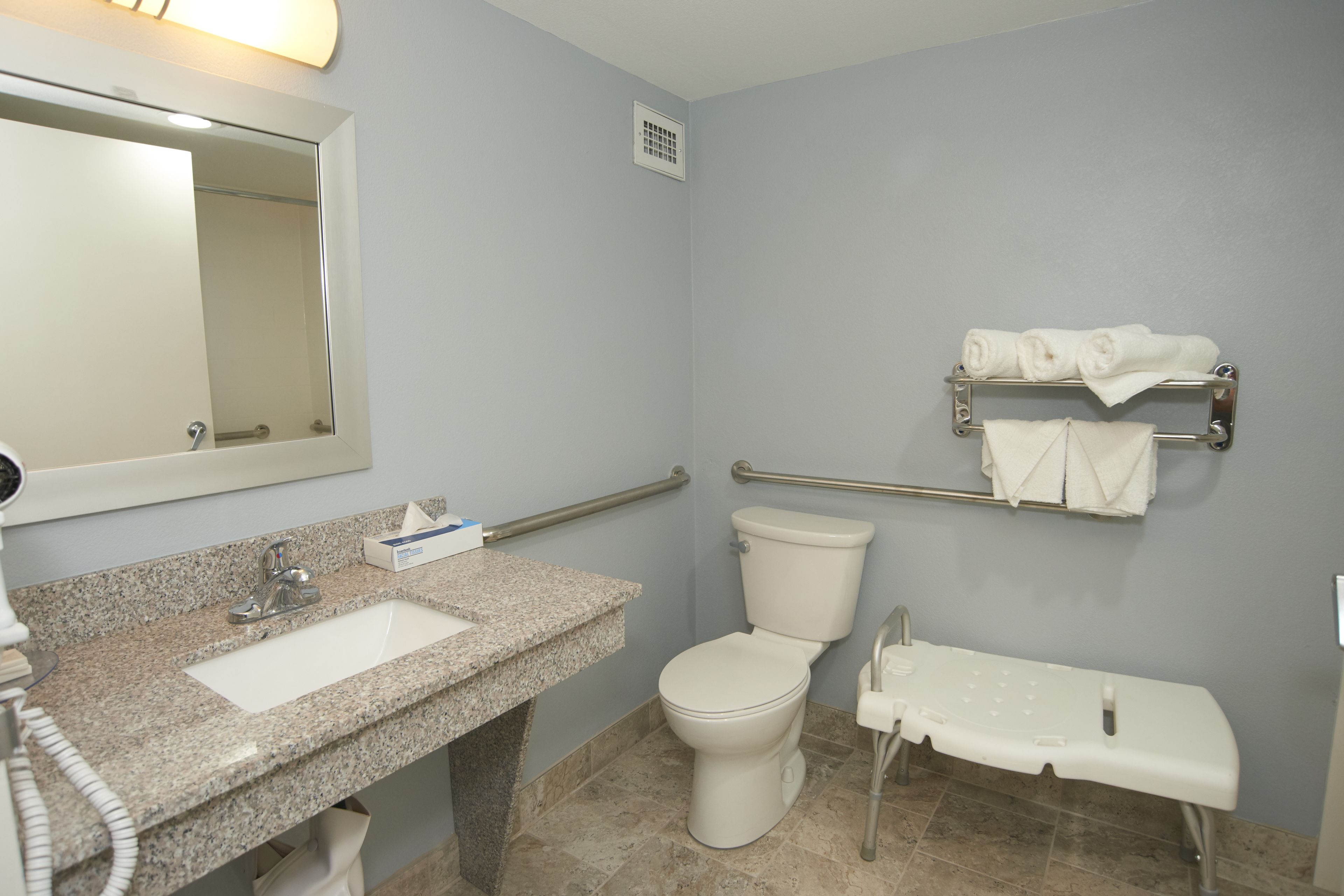 Un baño con lavamanos de granito, inodoro blanco y barra de apoyo.