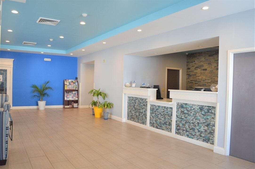 A reception area with a blue wall, a reception desk, and potted plants.
