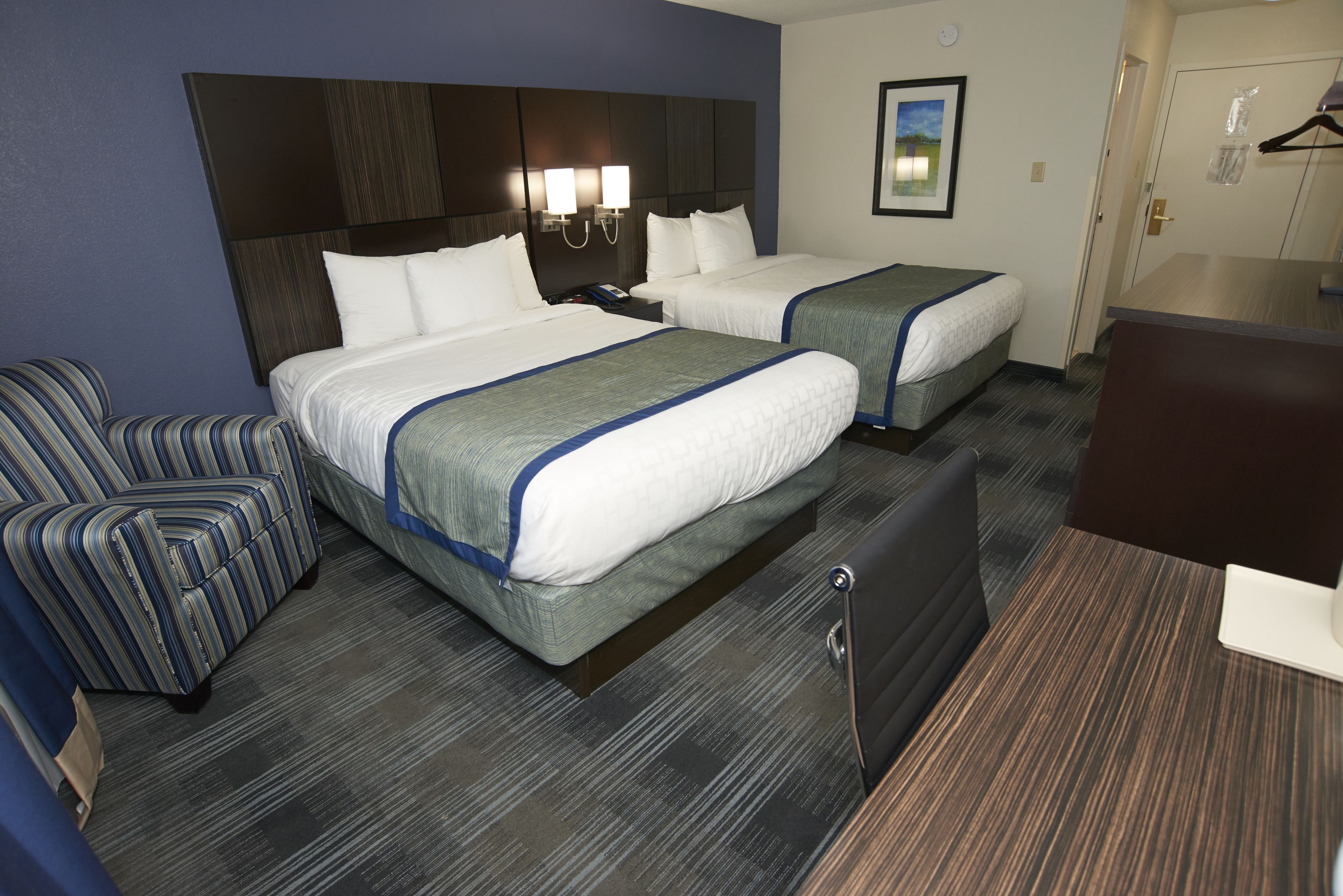 A hotel room with two beds, a desk, a chair, and a coat rack.