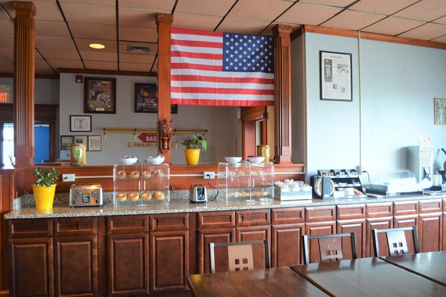 A breakfast bar with a large American flag, a coffee machine, and a display of pastries.