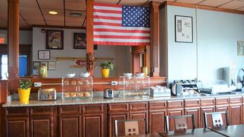 A breakfast bar with a large American flag, a coffee machine, and a display of pastries.