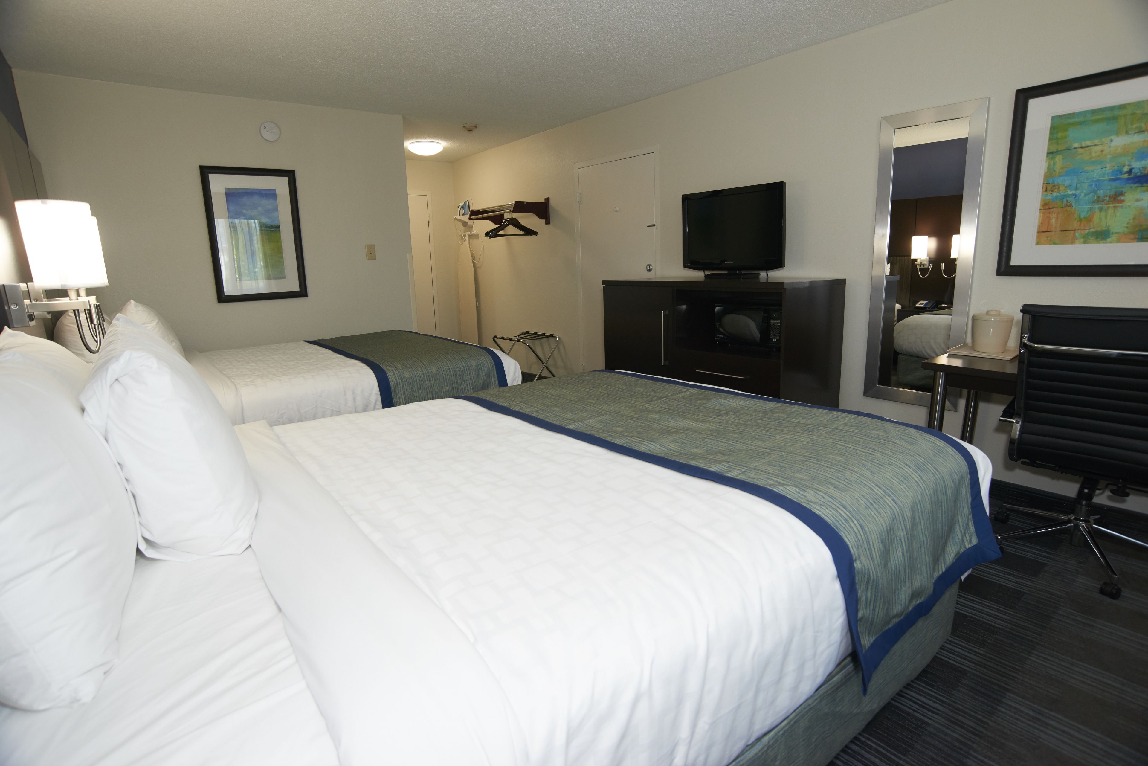 A hotel room with two beds, a television, a desk, and a chair.