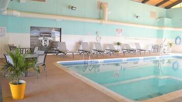 An indoor swimming pool with lounge chairs, a table with chairs, and a menu board advertising Flynie's Bar.