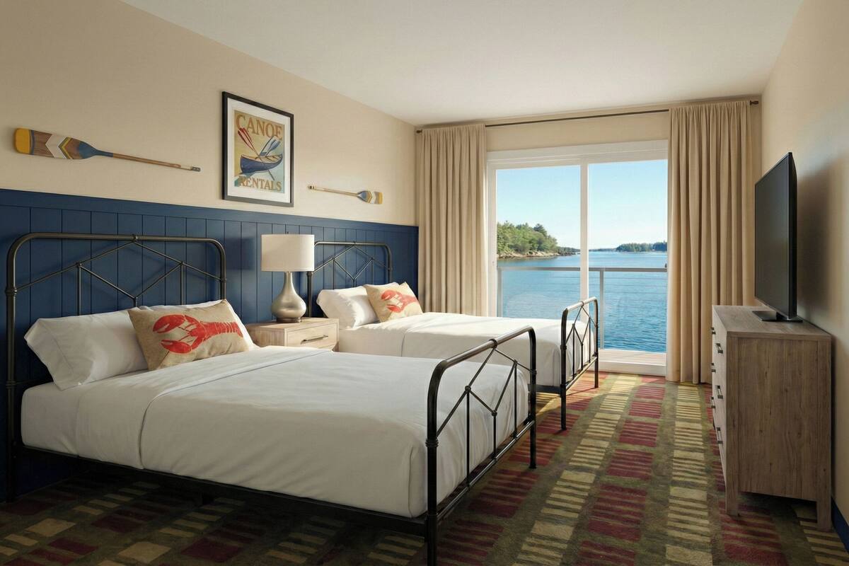 A hotel room with two beds, a television, a window with a view of the water, and a framed picture on the wall.