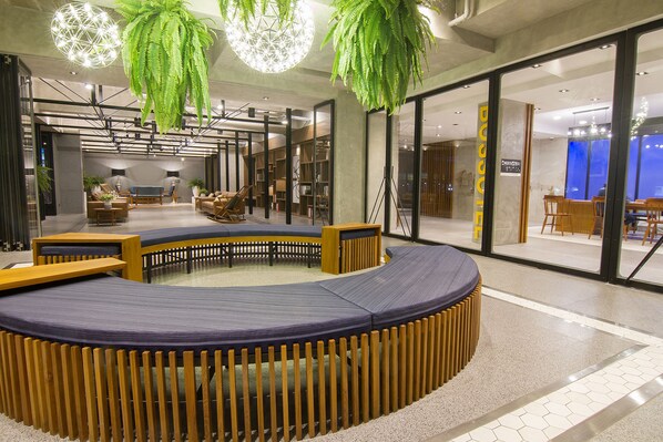 A modern indoor space with a circular seating area, wooden accents, and hanging green plants.