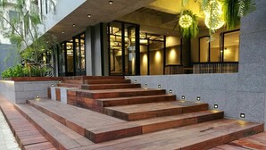 Un edificio moderno con una escalera que lleva a una entrada cubierta, zona de estar al aire libre y una lámpara colgante.