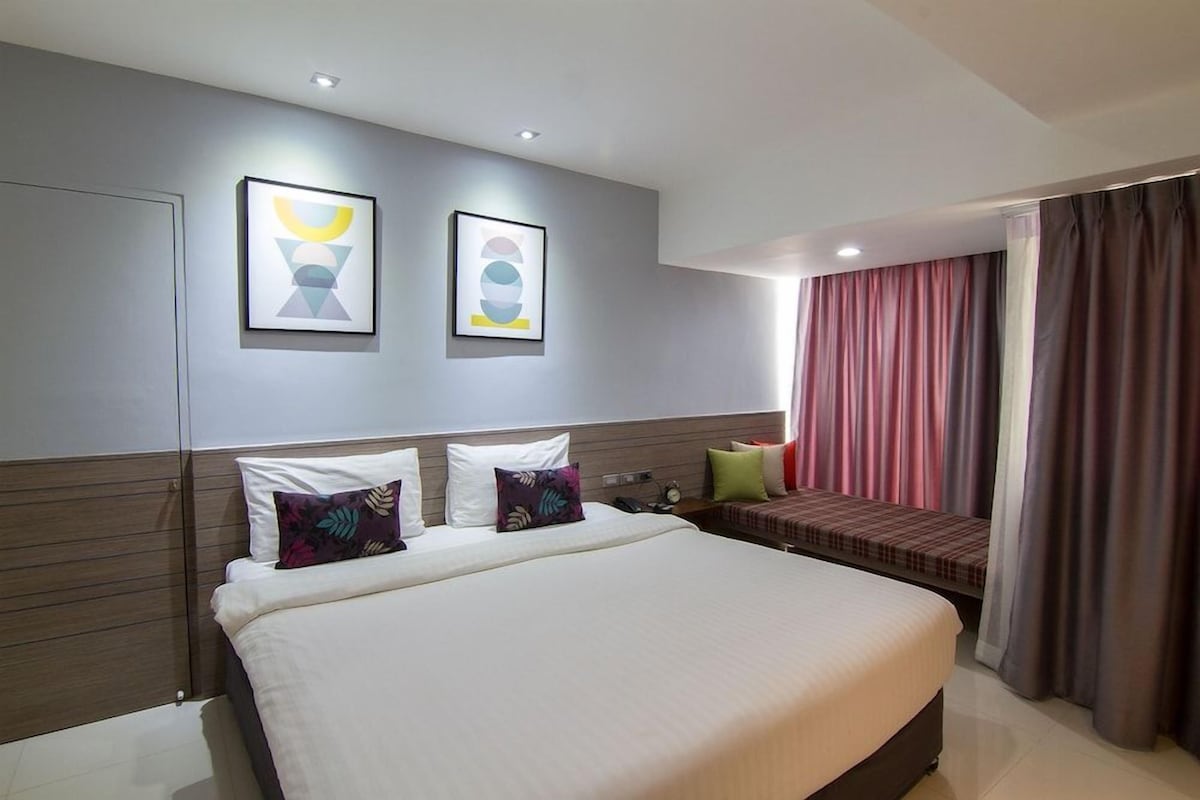 A modern hotel room with a large bed, a bedside table, and two framed artworks on the wall.