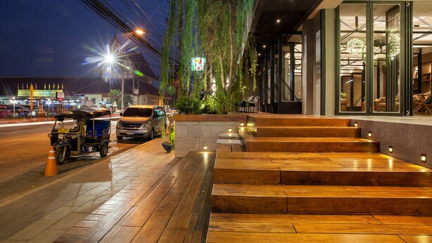 Un edificio moderno con una escalera de madera que conduce a una entrada, rodeado de vegetación e iluminado con luz ambiental.