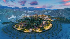 A resort with a central building surrounded by palm trees and desert landscape.