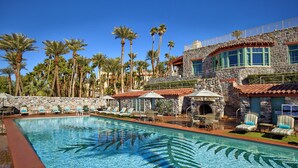 A pool area with lounge chairs, a stone building with a red-tiled roof, and palm trees.