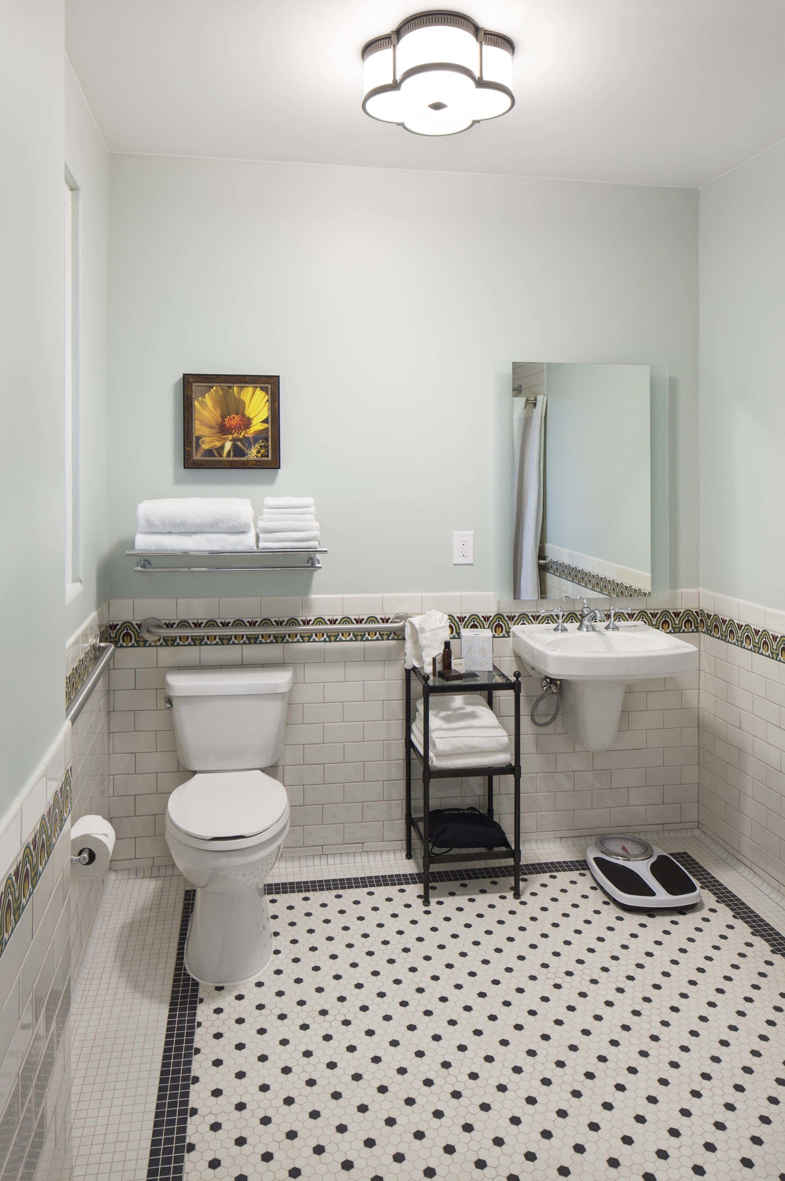 A bathroom with a toilet, sink, and shower area. There is a scale on the floor and a towel rack with towels.