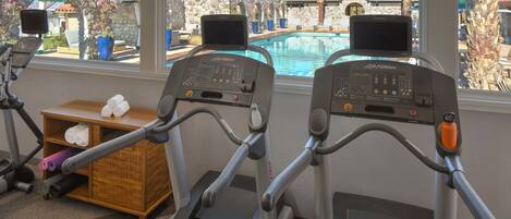 Two treadmills with a stone wall and a wooden shelf with towels.