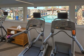Two treadmills with a stone wall and a wooden shelf with towels.