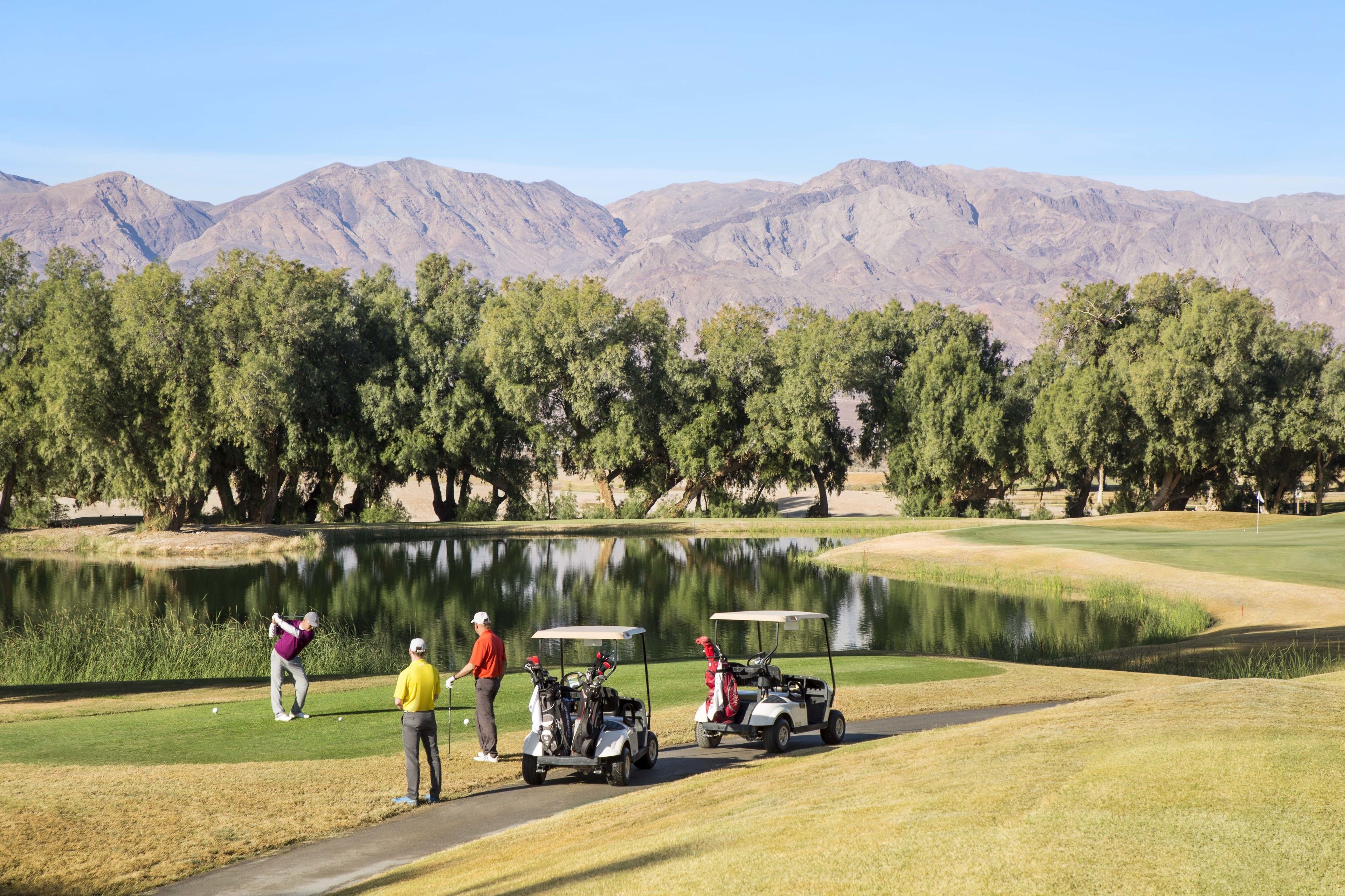 A golf course with a lake, trees, and mountains in the background.