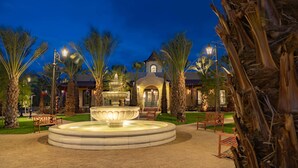 A well-lit fountain surrounded by palm trees and benches in a landscaped area.