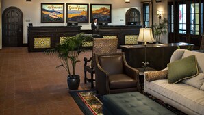 A lobby with a reception desk, framed artwork, a potted plant, a sofa, and a patterned rug.